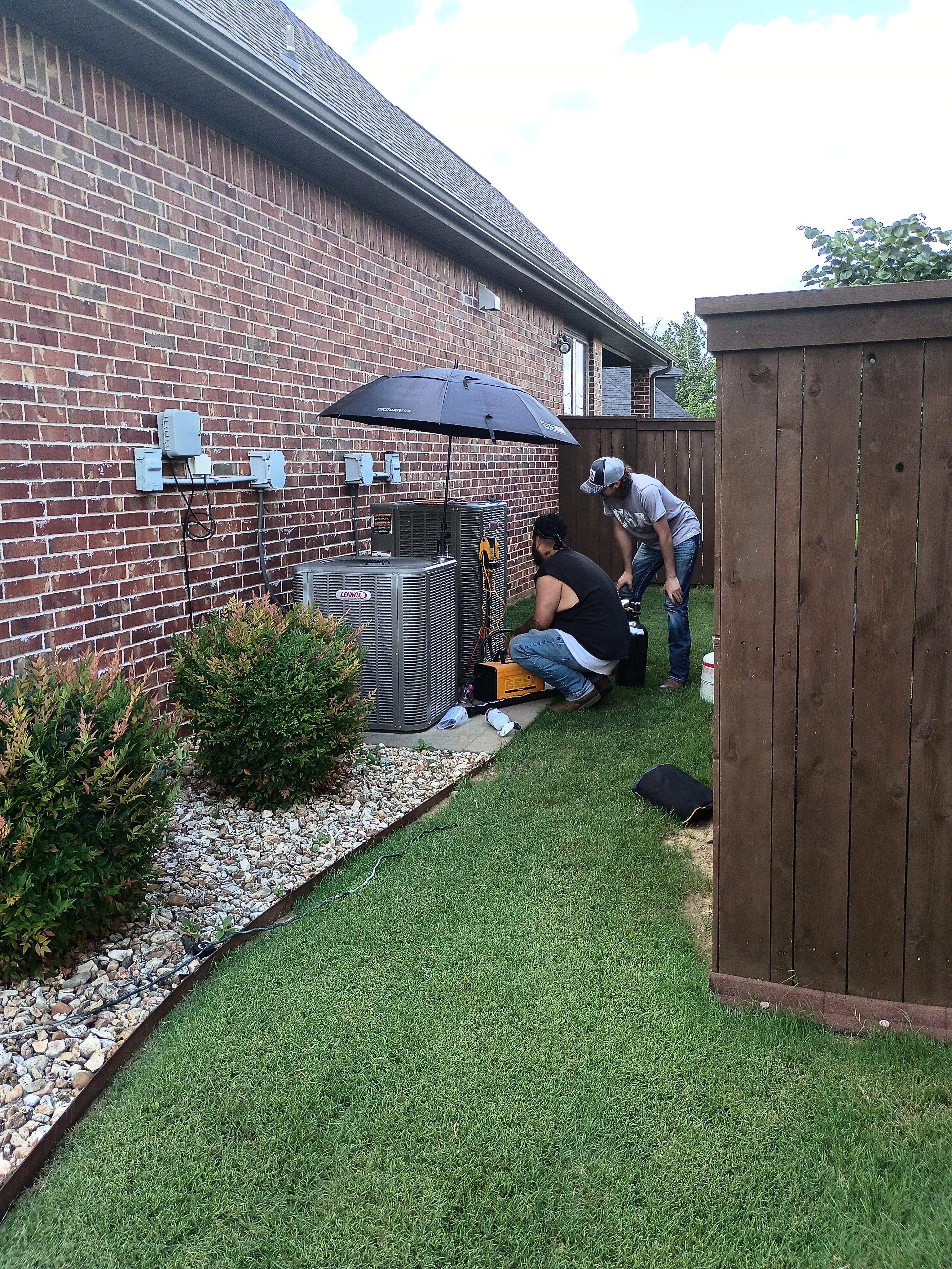 HVAC technicians installing residential air conditioning condenser unit on brick home